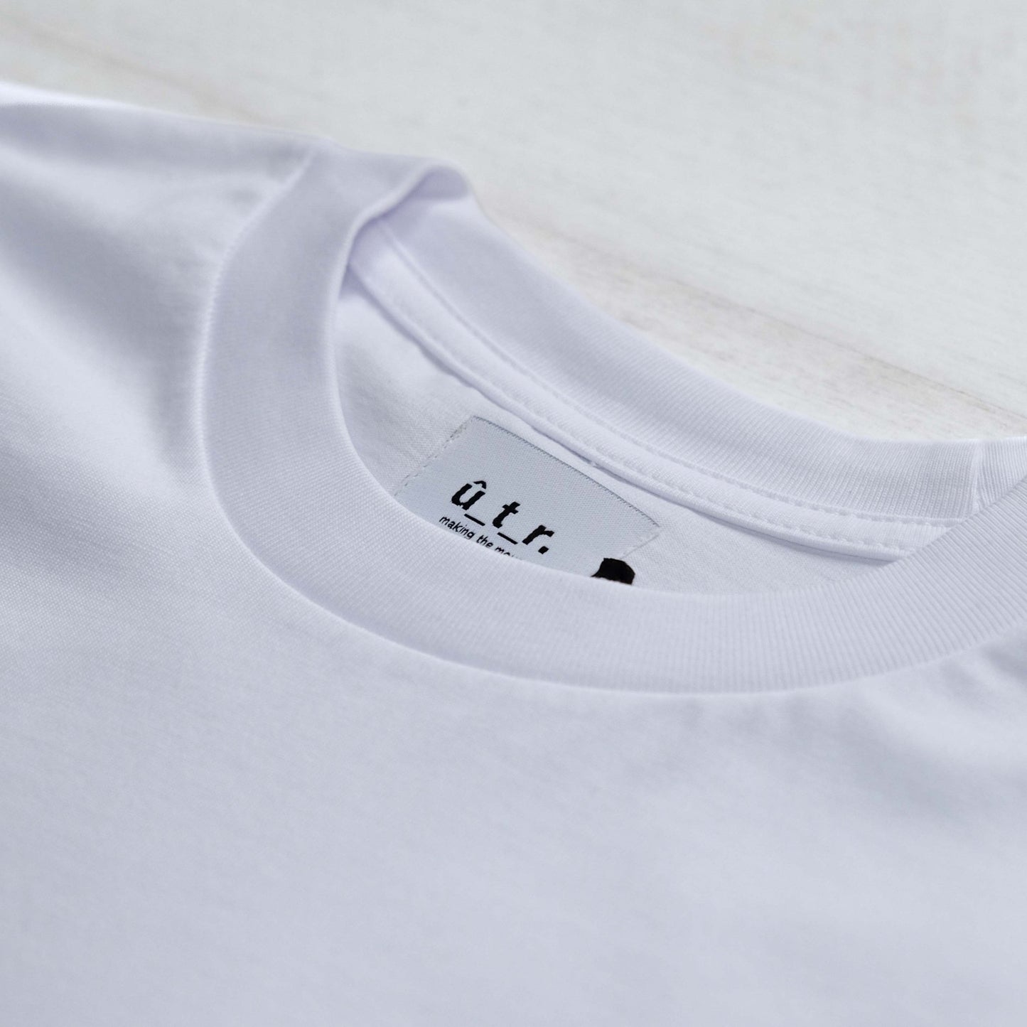 Neck of white t-shirt showing stitched in embroidered tag #negative space# - #Up The Road#